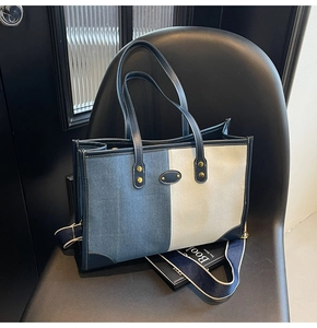 Detailed view of color-block denim tote bag with striped strap on a minimalist chair