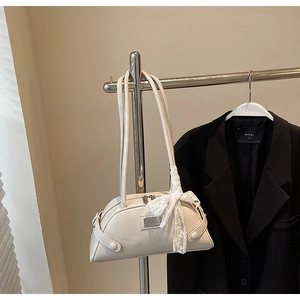 Close-up of cream bowling bag with lace bow hanging on metal rack with black blazer