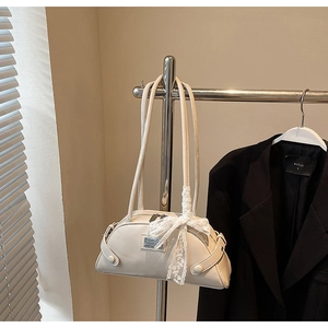 Detail view of cream bowling bag featuring silver plaque and delicate white lace bow