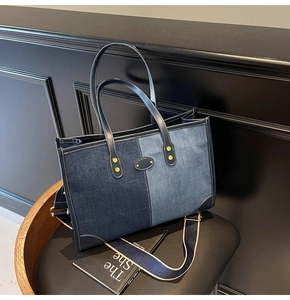 Detail of patchwork denim tote bag with leather handles and oval metal logo on leather seat