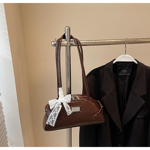 Detail of a brown vintage leather shoulder bag with white lace bow and metal logo plate