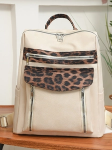 Large beige leopard print backpack with multiple zipper pockets on wooden table
