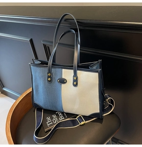 Detail of a denim contrast tote bag with leather trim and gold rivets on a dark chair