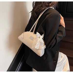 Detail of cream baguette shoulder bag featuring a lace bow and metal plaque accent
