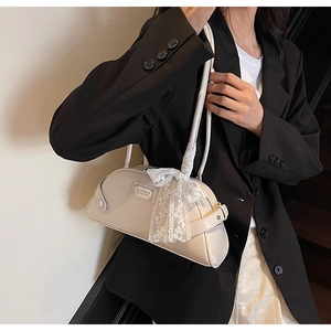 Close-up of cream bowling bag with lace bow and MINO metal plate on black blazer