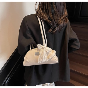 Cream-colored shoulder bag with lace bow and metal plaque shown on a model