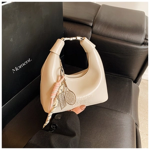 Détail du sac hobo beige avec pendentif tressé et breloque raquette de tennis en métal