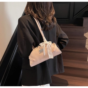 Detail of light pink shoulder bag featuring a lace bow and silver metal nameplate