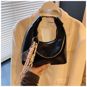 Détail du sac croissant noir verni avec boucle argentée et breloque de raquette de tennis