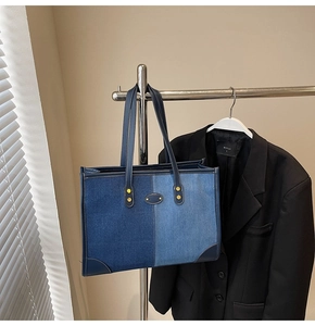 Detail of color-block denim tote bag with golden rivets and metallic logo plate
