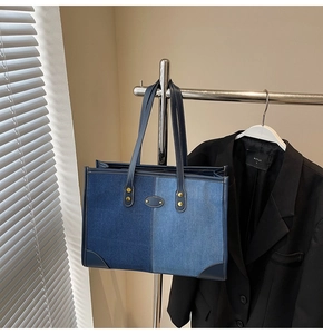 Detail of blue patchwork denim tote bag featuring white stitching and leather handles