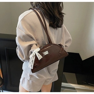 Detail of dark brown patent leather bowling bag with white lace bow and metal plaque