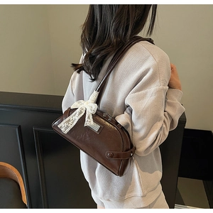 Detail of a brown leather baguette bag featuring a white lace bow and metallic logo plate