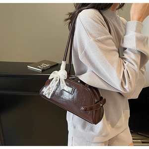 Detail of dark brown glossy leather bowling bag with white lace bow and silver logo