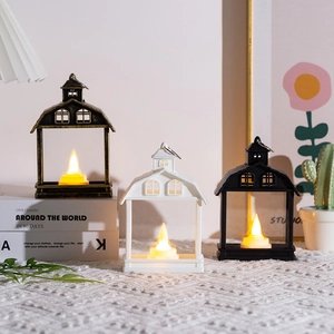Detailed view of three decorative house-shaped LED candle lanterns in black, white, and bronze