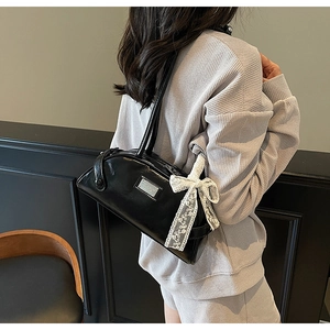 Detail of black glossy leather baguette bag with silver plate and lace bow decoration