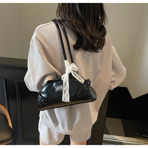 Detail of black glossy leather bowling bag featuring a white lace bow and metal logo plate