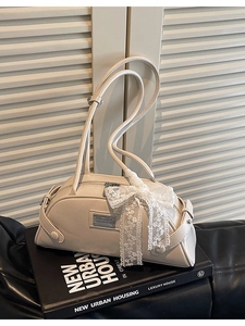 Elegant cream bowling shoulder bag with lace bow detail and metal plaque on urban book