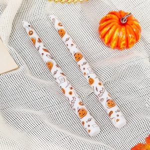 Pair of white Halloween taper candles featuring festive pumpkin and bat print patterns