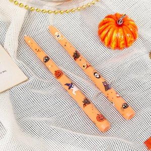 Two orange 25cm Halloween pillar candles with pumpkin and bat prints on white fabric
