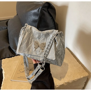 Detail of silver pleated shoulder bag featuring a metallic butterfly buckle and chain strap