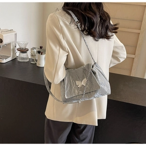 Detail of silver tote bag with crinkled metallic texture and butterfly ornament charm