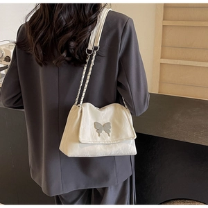 Detail of white tote bag featuring silver butterfly clasp and metal chain shoulder strap