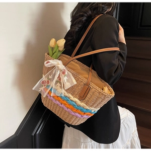 Detail view of woven straw tote bag featuring colorful stripes and white lace flower embroidery