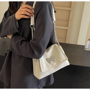 Close-up of white tote bag with silver butterfly emblem and metal chain strap