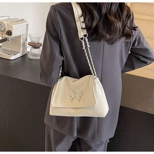 Detail of ivory tote bag with silver butterfly charm and chain strap on shoulder