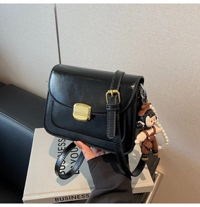 Detail of black crossbody bag with golden lock, pearl chain and cartoon doll charm