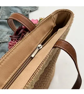 Detail of a woven straw tote with smooth metal zipper and brown leather handle contrast