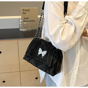 Detail of black pleated tote bag with white butterfly charm and metal chain strap