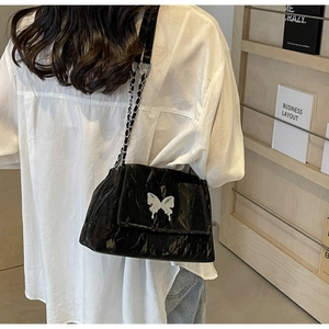 Detail of black leather shoulder bag with silver butterfly buckle and chain strap