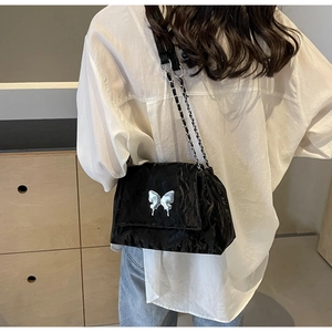 Close-up of black pleated leather tote bag with silver butterfly and chain strap