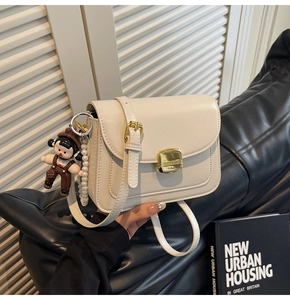 Close-up of beige square bag with gold lock, pearl chain, and cartoon charm detail