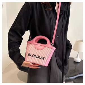Detalle de bolso tipo cubo rosa tejido con correa de cuero llevado por modelo en negro