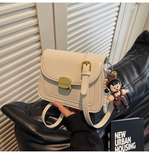 Detail of cream leather flap bag featuring golden square lock and pearl charm accessory