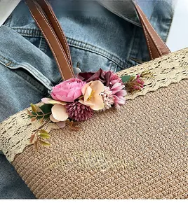 Detail of straw woven tote bag featuring decorative 3D flowers and lace trim