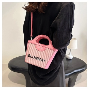 Detalle de bolso tipo cubo de tejido rosa con asas de cuero y correa de hombro