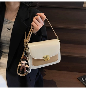 Detail of a two-tone crossbody bag with gold buckle and pearl doll charms on steps