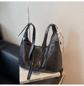Detail of black pleated tote bag with woven tassels and silver hardware on books