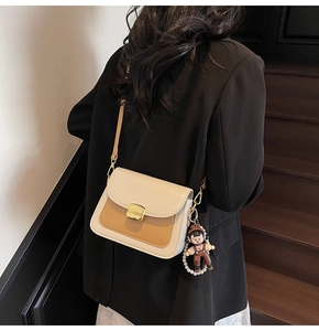 Detail of beige and khaki leather crossbody bag with gold buckle and pearl chain charm