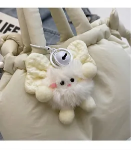 Primer plano de un colgante de peluche blanco con lazo amarillo y cascabel en un bolso beige