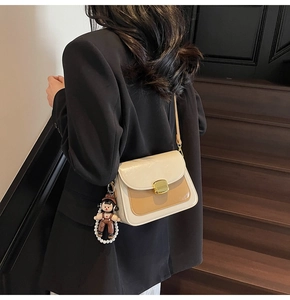 Detail of two-tone beige and khaki crossbody bag with doll pendant on a model
