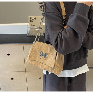 Close-up of khaki tote with pleated texture, liquid silver butterfly, and chain strap