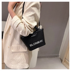 Vista lateral del bolso tote negro tejido con correa ajustable usado por modelo