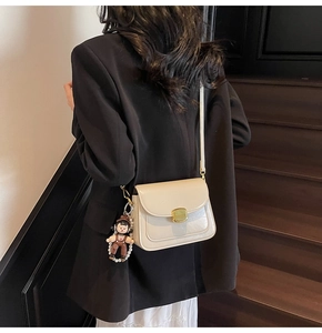 Close-up of minimalist cream crossbody bag with gold buckle and pearl doll charm