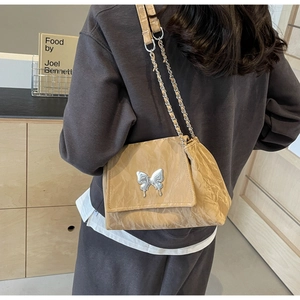 Detail of khaki pleated tote bag featuring a large silver butterfly metal buckle and chain strap