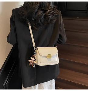 Chic cream leather square bag shown crossbody with a cute doll charm detail